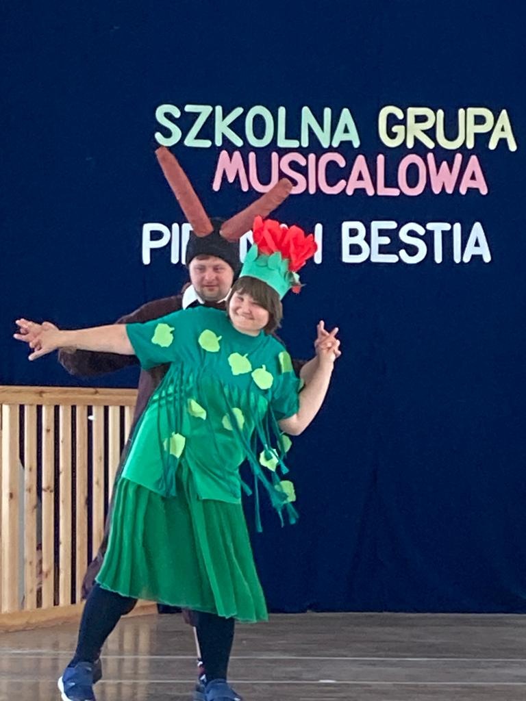Na scenie w auli szkolnej tańczy dwoje aktorów musicalu "Piękna i Bestia"
