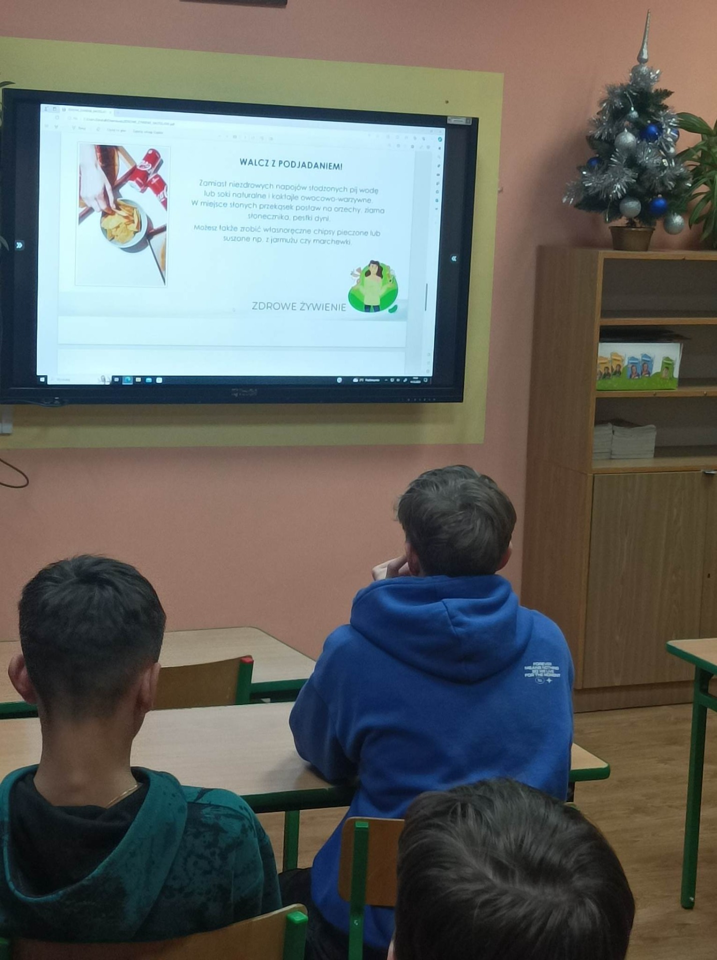 Uczniowie oglądają na lekcji prezentację o zdrowym żywieniu wyświetlaną na monitorze interaktywnym.