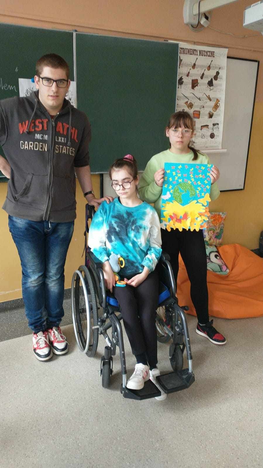 3 uczniów, w tym 1 na wózku prezentuje plakat dotyczący plenety Ziemia