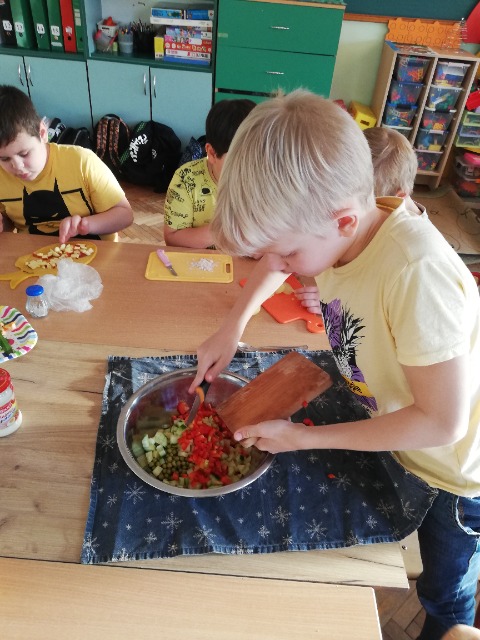 Uczeń zrzuca z deski do miski pokrojone warzywa.