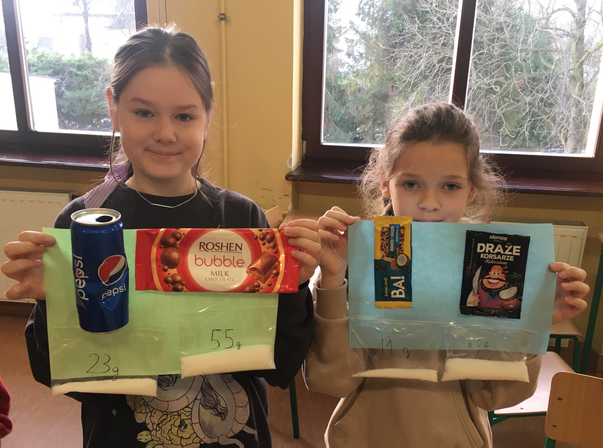 Na zdjęciu uczniowie prezentują swoje wykonane plakaty, które przedstawiają zawartość cukru w przekąskach i napojach.