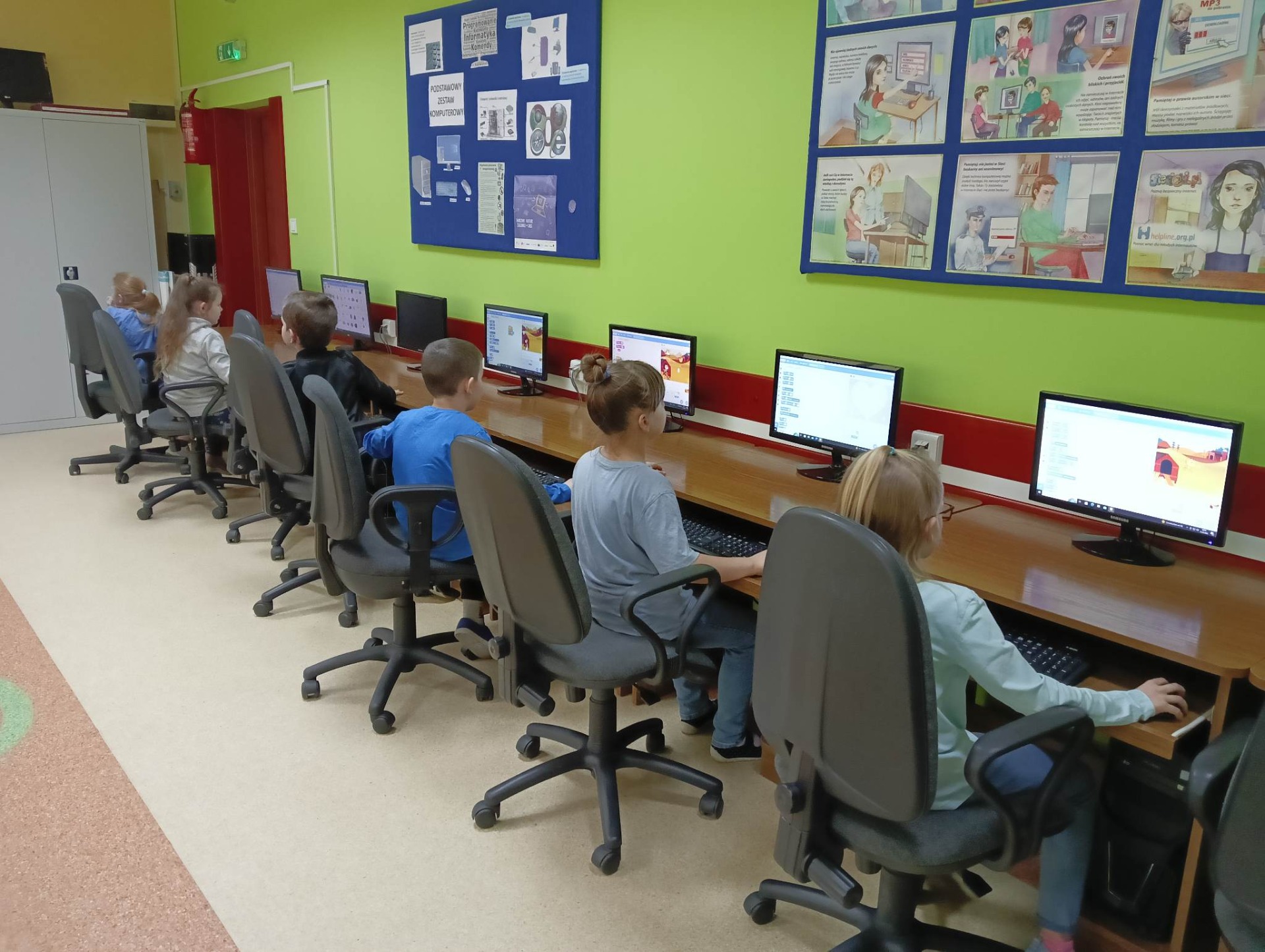 Uczniowie siedzą przy stanowiskach komputerowych w sali informatycznej