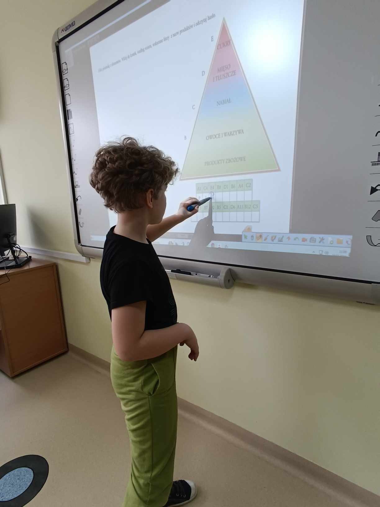 Uczeń układa piramidę żywieniową na tablicy multimedialnej.