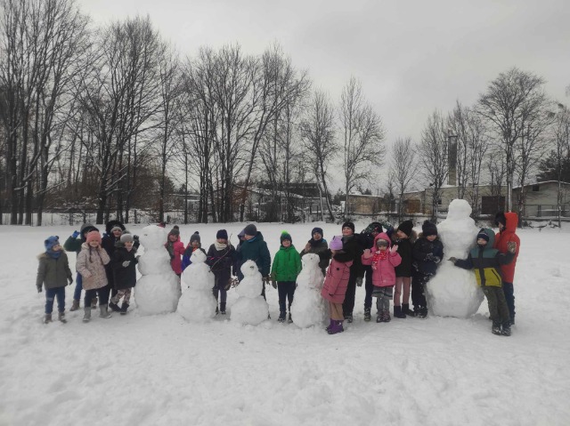 grupa dzieci stoi przy ulepionych bałwanach ze śniegu