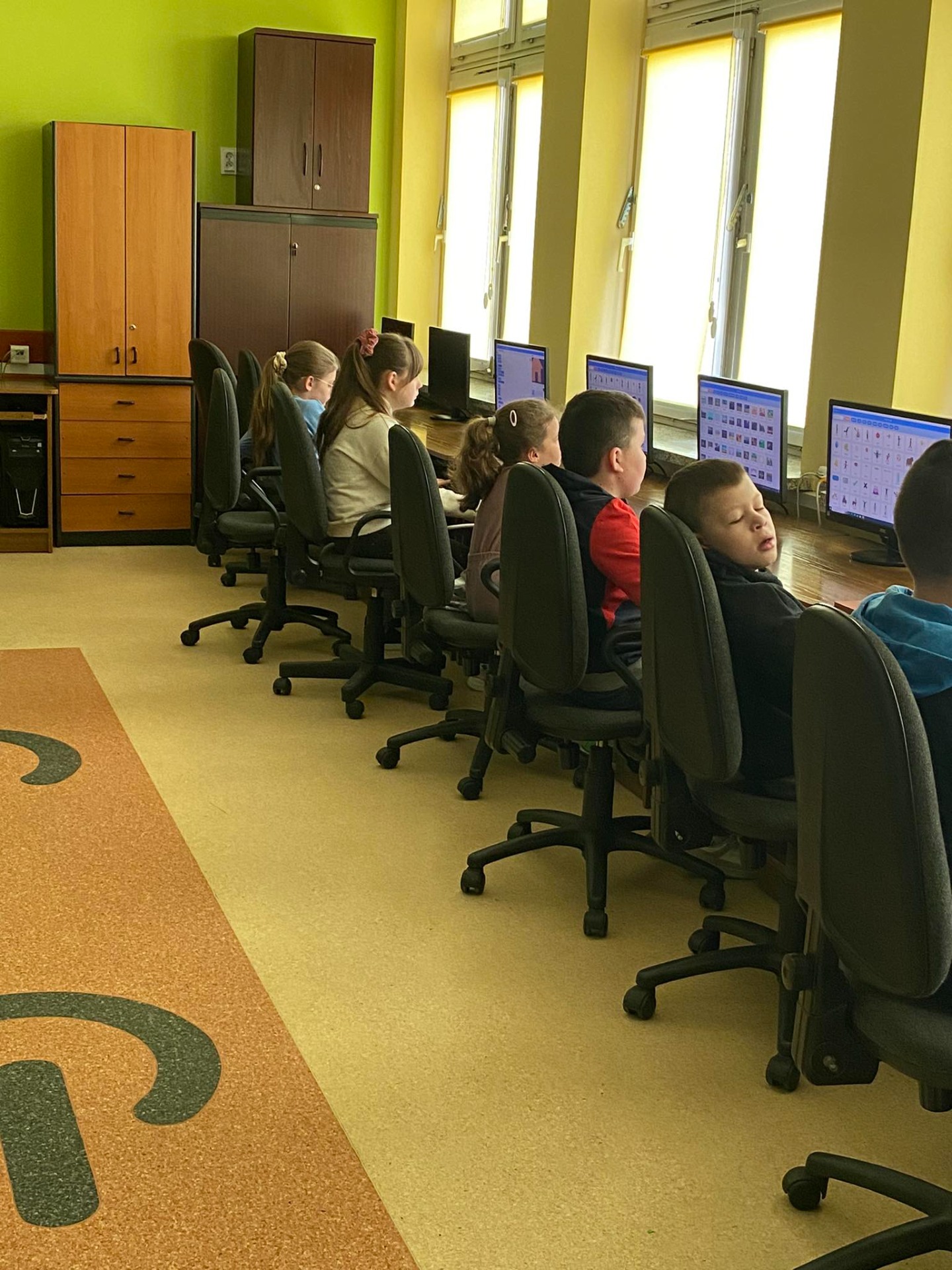 Uczniowie siedzą przy komputerach w sali informatycznej i tworzą animacje w programie Scratch